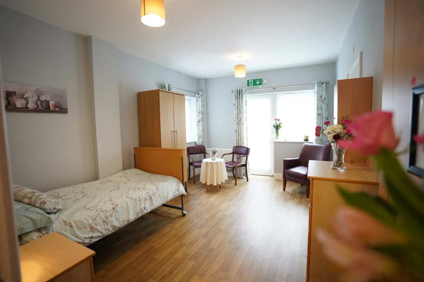 A bedroom with a made bed, wardrobe, armchairs and patio doors to the garden